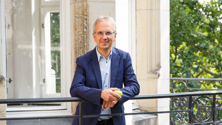 Prof. Dr. Andreas Michalsen auf dem Klinikbalkon mit einem Apfel in der Hand, Abteilung für Naturheilkunde am Immanuel Krankenhaus Berlin